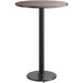 A round Lancaster Table & Seating bar table with a black metal base and a reversible wood table top.