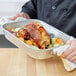 A person holding a Vollrath aluminum roasting pan with a roast chicken.