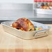A Vollrath aluminum roasting pan with a roast chicken in it.
