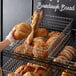 A hand placing a loaf of bread in a Choice wire basket on a bakery counter.