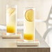 Two glasses of Les Vergers Boiron Mirabelle Plum fruit drinks on coasters.