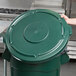A hand holding a green Rubbermaid BRUTE trash can lid.