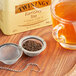 Loose dried Twinings Earl Grey tea leaves in a strainer over a glass mug of tea.
