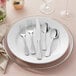 A white plate with Acopa Triumph stainless steel flatware on it.