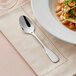 An Acopa Triumph stainless steel teaspoon on a napkin next to a bowl of soup.