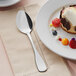 A plate with dessert on it next to an Acopa Triumph stainless steel dessert spoon.