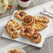 A plate of Schulstad large assorted Danish pastries on a table with a white cup of coffee.