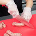A person using a Mercer Culinary Millennia Colors® chef knife to cut sausages on a red cutting board.