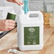 A hand pouring Noble Eco Novo Terra hand and body lotion from a green and white bottle into a white plastic container.