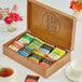 A Bigelow wooden tea chest open to reveal 8 compartments filled with assorted tea bags.