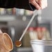 A person using a Vollrath long handled measuring spoon to stir brown powder in a bowl.