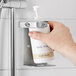 A hand holding a white Novo by Noble Chemical bottle of soap over a shower.