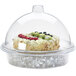 A Cal-Mil clear dome covering a cake with ice and berries on top.
