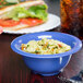 A peacock blue melamine bowl of pasta and a sandwich on a table.