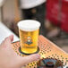 A hand holding a glass of beer on a metal table outdoors.