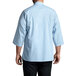A man wearing a sky blue Uncommon Chef 3/4 sleeve chef coat with side vents.