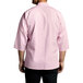 A man wearing a pink Uncommon Chef 3/4 length sleeve chef coat with black pants.