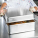 A chef using a Vollrath aluminum roasting pan with food inside.