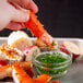 A hand holding a Chesapeake Crab Connection large Alaskan king crab leg over a bowl of sauce.