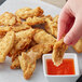 A hand dipping a Daring Foods breaded chicken strip into sauce.