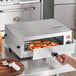 A hand using a Carnival King countertop pizza oven to cook a pizza.