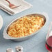 A Choice stainless steel oval au gratin dish with food on a table.