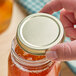 A hand holding a jar with a 63/400 gold metal lid containing honey.