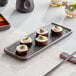 A black Acopa Heika stoneware plate with sushi on it.