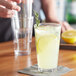 A hand pouring lemonade into an Acopa Select stackable glass with ice and lemon slices.