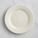 An Acopa Swell ivory stoneware plate with an embossed design on the rim.