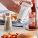 A hand using a Choice mushroom top salt shaker to sprinkle salt on a burger.