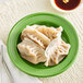 An Acopa Capri palm green stoneware plate with dumplings and chopsticks on a white place mat.