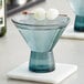 A blue Acopa Pangea martini glass with liquid and two round ice balls in it.