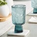 An Acopa Pangea blue goblet filled with ice water on a table with a coaster.