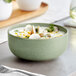 A close-up of a sage matte porcelain bowl filled with soup, clams, and herbs.