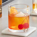 An Acopa Pangea rocks glass with orange liquid and cherries.