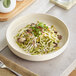 A bowl of pasta with mushrooms and sprouts in an Acopa Pangea fog white matte porcelain pasta bowl on a table.