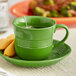 An Acopa Capri palm green stoneware cup on a plate with a tea bag.