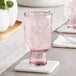An Acopa mauve goblet filled with ice water on a white coaster.