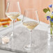 Two Acopa Silhouette wine glasses on a marble table with white wine and flowers.