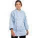 A woman wearing a sky blue Uncommon Chef Orleans long sleeve chef coat with buttons and pockets.