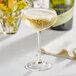 An Acopa Select coupe glass of champagne on a table with a bottle and flowers.