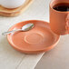 An Acopa Terra Cotta porcelain saucer with a cup of coffee and a spoon on a table.