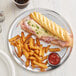 A close up of a Choice aluminum wide rim pizza pan with a sandwich and french fries on it.