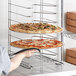 A person holding a pizza on a Choice aluminum wide rim pizza pan rack.