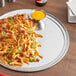 A stack of Choice 16" Aluminum Wide Rim Pizza Pans on a table with a plate of french fries with jalapenos and cheese.