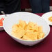 A white slanted melamine bowl of chips on a table.
