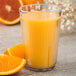 A Carlisle clear plastic tumbler filled with orange juice and slices of orange on the side.