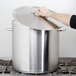 A person holding a Vollrath Centurion stainless steel stock pot lid over a large silver pot.
