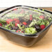 A Sabert clear plastic bowl with a lid containing a salad with strawberries and greens.